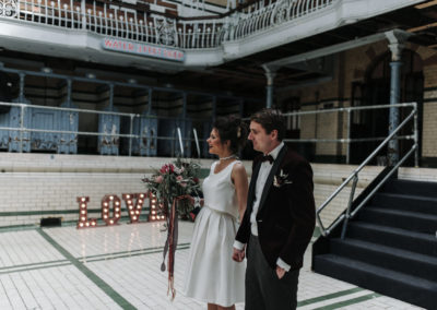 bride and groom walk past light up love sign at victoria baths in Manchester
